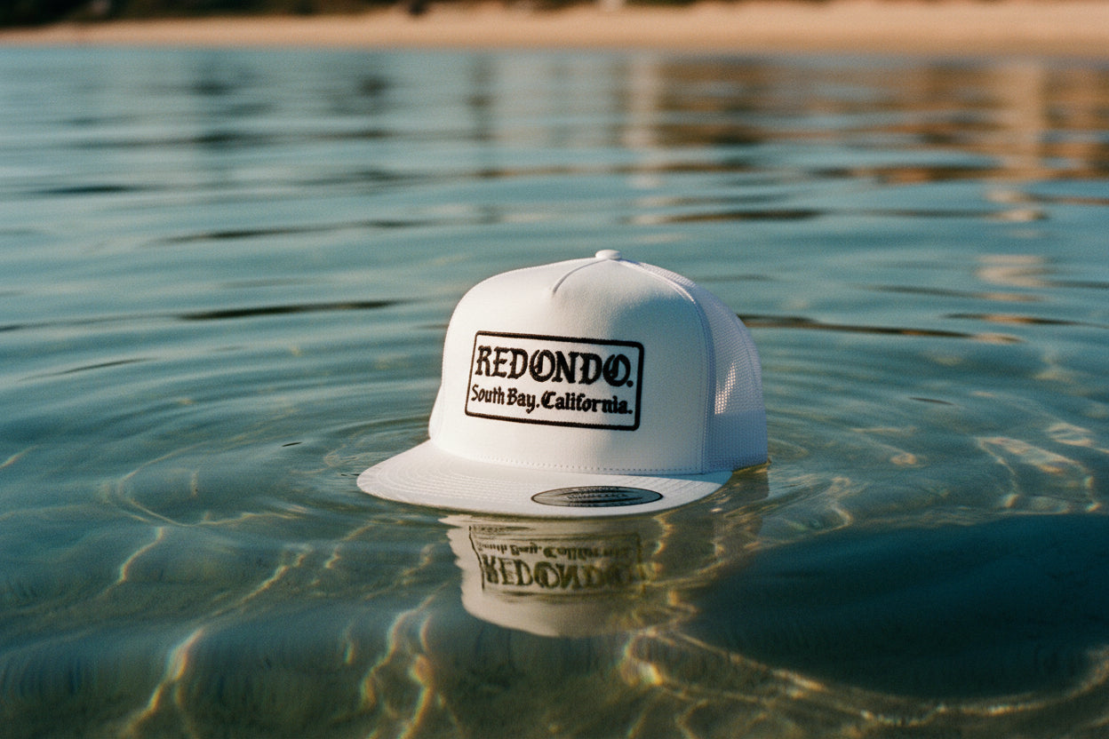 White cap with 'Redondo, South Bay, California' text on a fluffy beige background