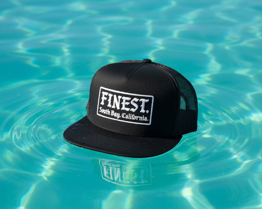 Black cap with 'Finest' logo on a textured beige surface