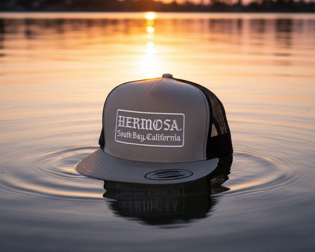 Gray and black cap with 'Hermosa' branding on a textured surface